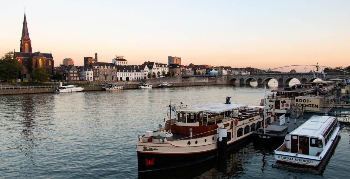 The Maas River with river boats and the stone Sint Servaasbrug in Maastricht, the Netherlands, at sunset