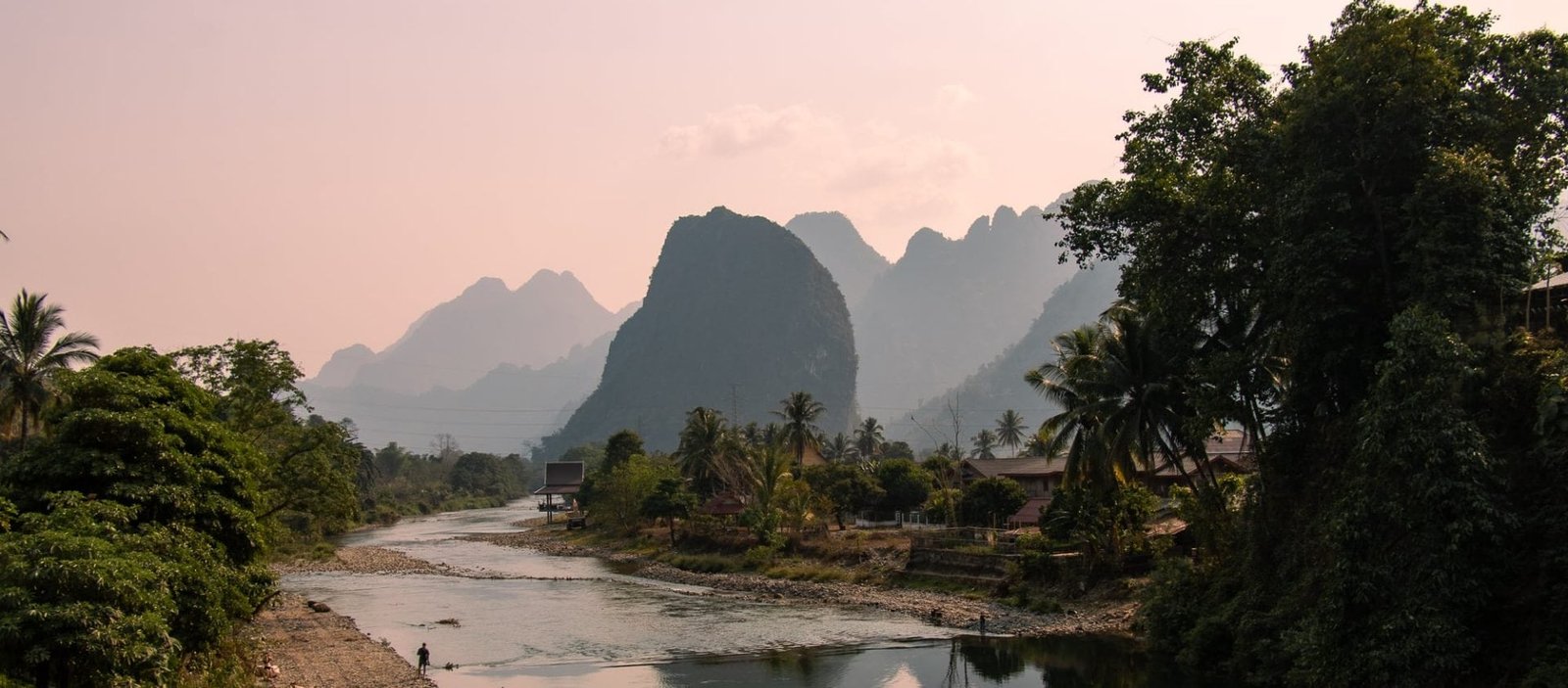 Sunset view over the rural landscapes of Laos with a river winding along limestone karst mountains and palmtrees