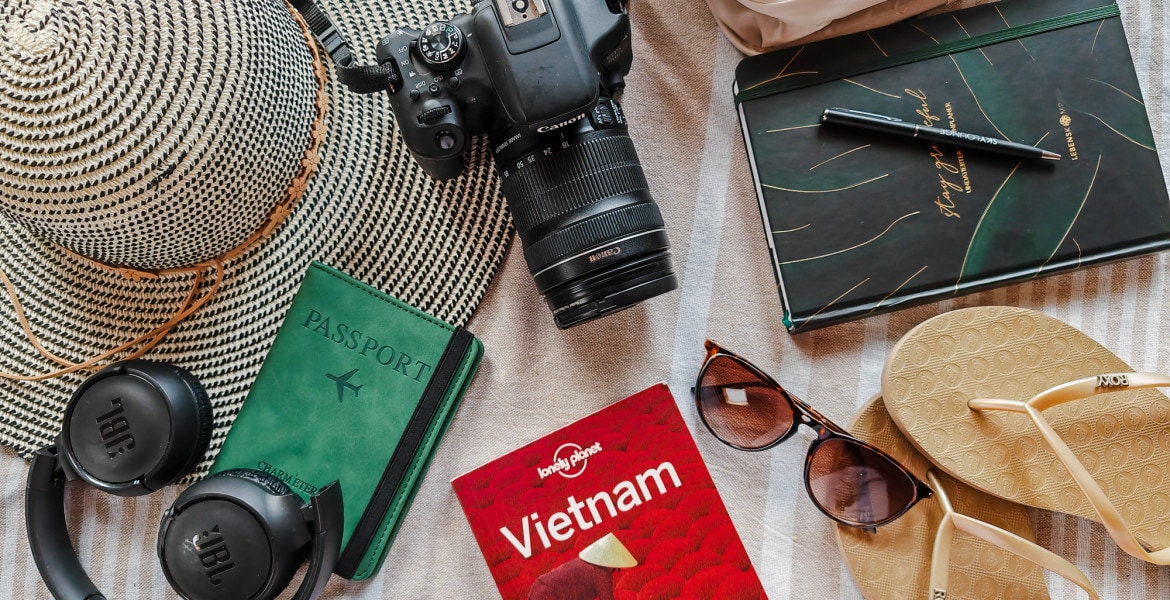 Flatlay of travel essentials for Vietnam Packing List such as a travel guide, sunglasses, passport, toiletries, camera gear and flipflops.