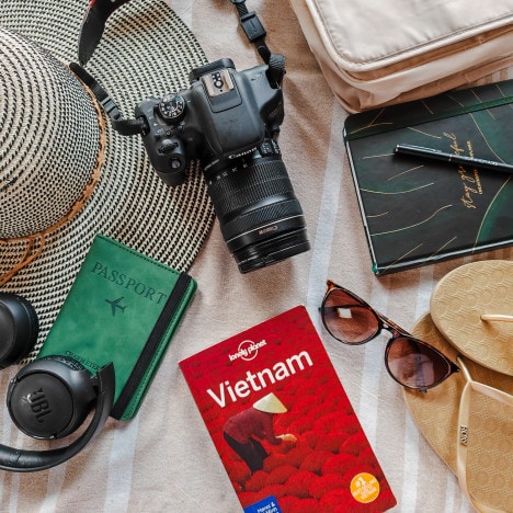 Flatlay of travel essentials for Vietnam Packing List such as a travel guide, sunglasses, passport, toiletries, camera gear and flipflops.