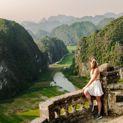 Sunrise view over a river surrounded by green rice paddies and towering limestone mountains from Hang Mua viewpoint in Ninh Binh, Vietnam.