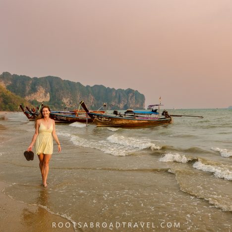 Girl walking on Ao Nang Beach in Krabi Thailand during sunset with longtail boats and limestone mountains in the back