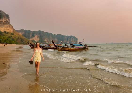 Girl walking on Ao Nang Beach in Krabi Thailand during sunset with longtail boats and limestone mountains in the back